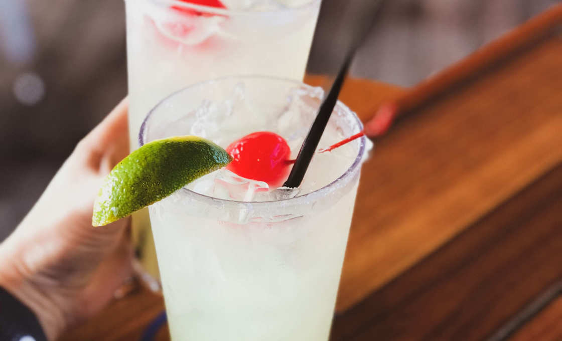 Two glasses of Almendra Colada on a wood table, with a hand reaching for one