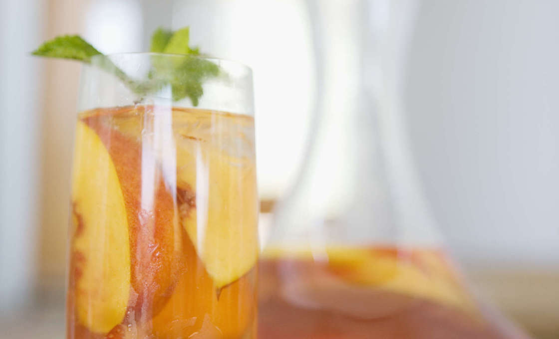 Tall glass of Peach And Bourbon Iced Tea with a jug behind