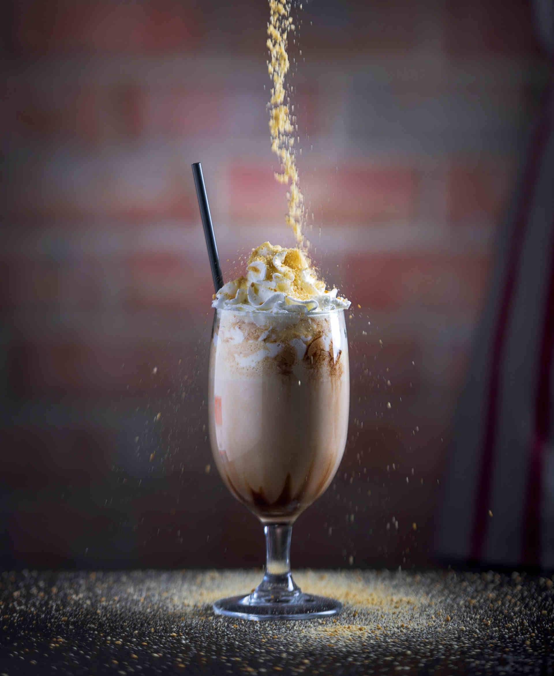 Pistachio pieces being sprinkled onto a glass of Popcorn Caramel Milkshake