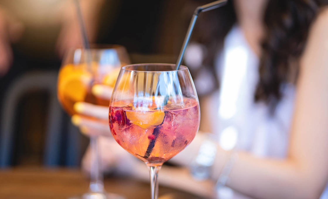 Glass of Cotton Candy Spritz with a woman holding a cocktail in the background