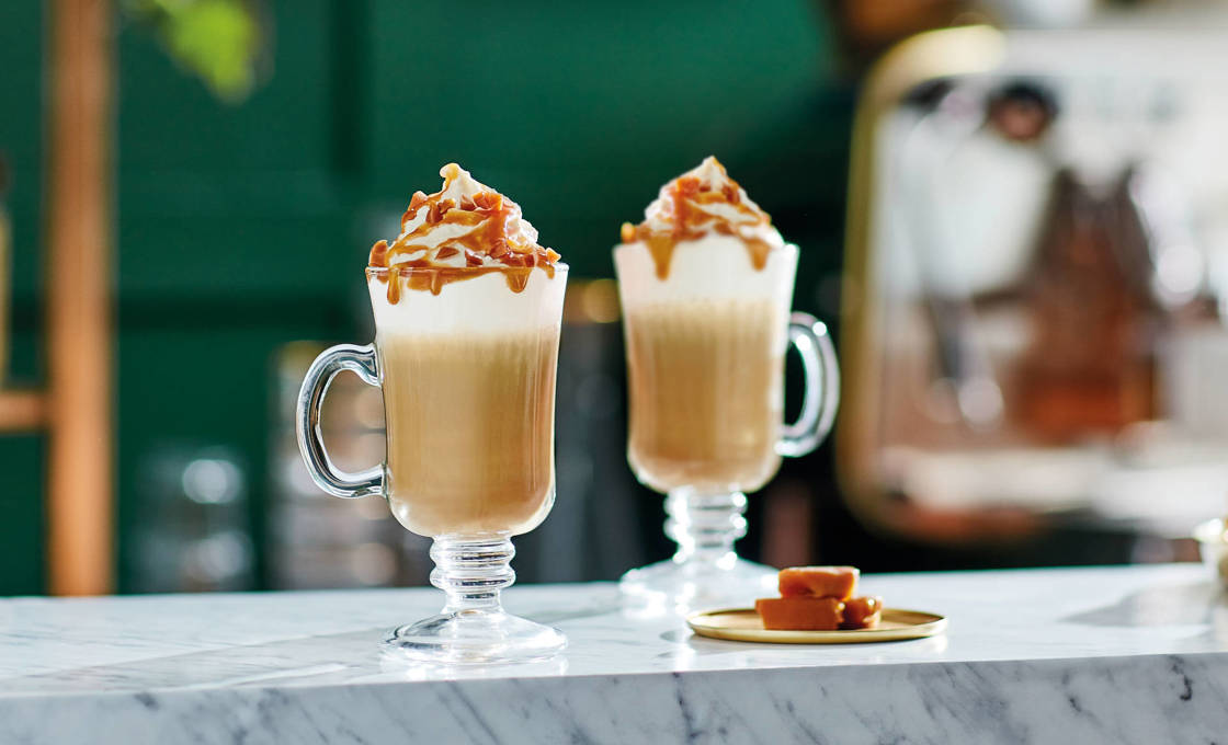 A glass of Iced Latte Deluxe with a straw and whipped cream on top