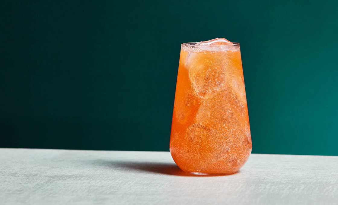 A glass of Orange Spritz Sparkling Lemonade on a table with a green background
