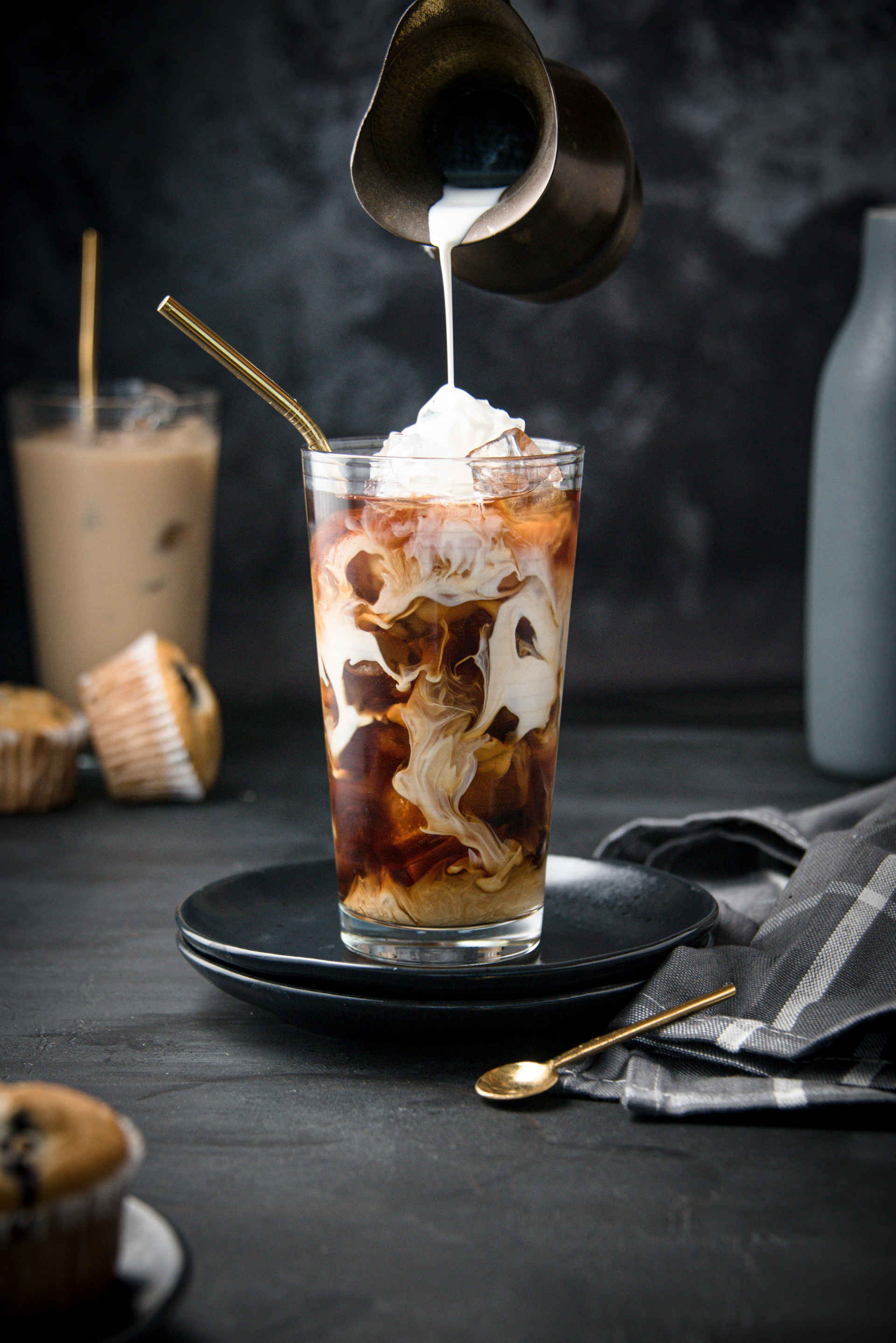 A Chestnut Iced Latte in a highball glass with milk being poured on top