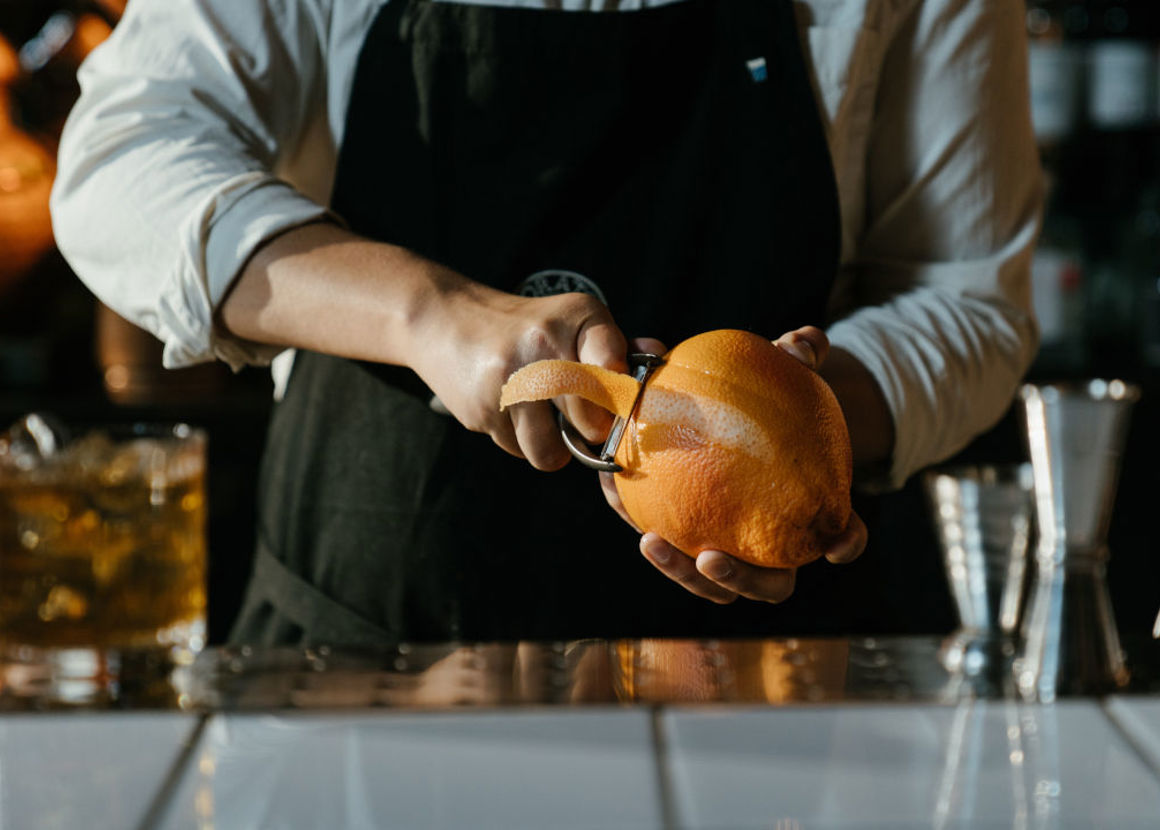 Person in White Long Sleeve Shirt and Apron peeling orange