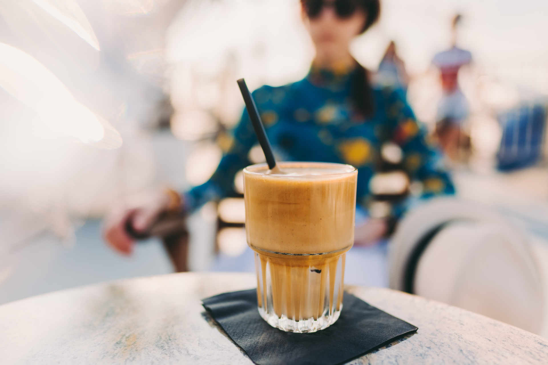 Glass of minty mocha on a table with a woman out of focus in the background